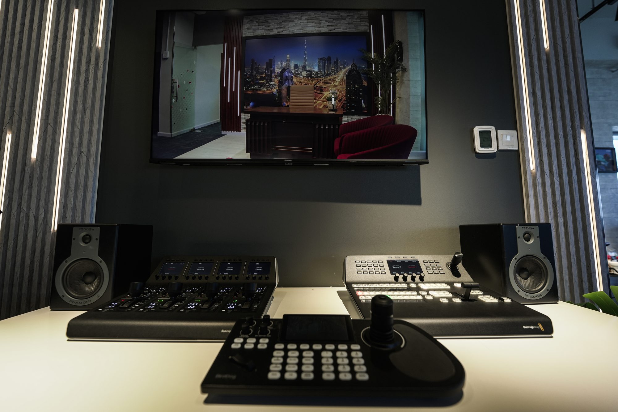 A PTZ joystick controller at the desk, the set on the screen behind